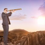 Businessman looking through telescope against clouds